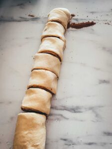 Der aufgerollte Zimtschneckenteig mit Füllung wird nun in 12 gleich große Stücke geschnitten.