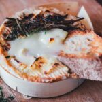 Gebackener Camembert aus der Heißluftfritteuse mit flüssigem Kern, getoppt mit geröstetem Rosmarin und serviert mit Baguette auf einem Holzbrett.