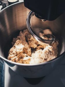 Nahaufnahme von unfertigem Hefeteig in einer Küchenmaschine, der gerade mit dem Knethaken bearbeitet wird.