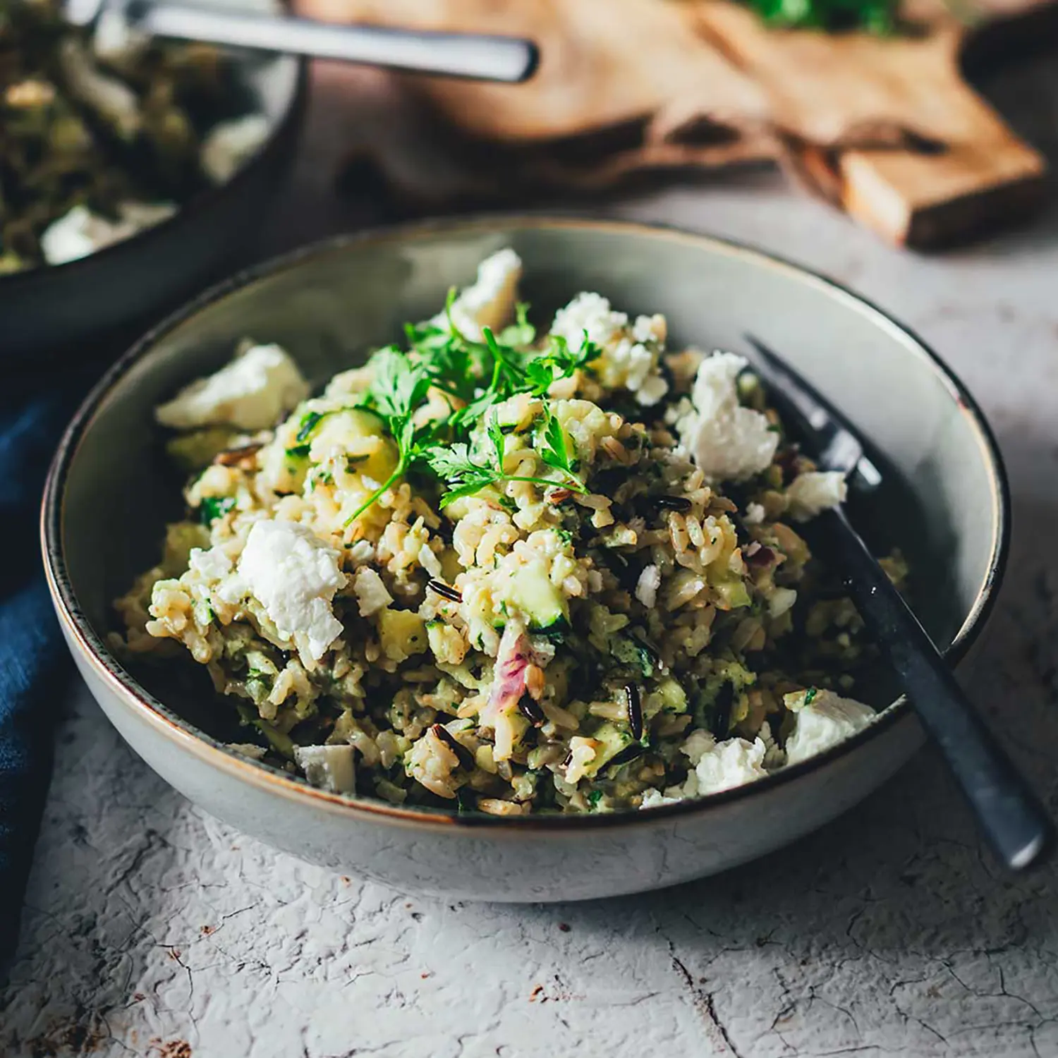 Angerichteter Teller mit Reissalat mit Zucchini und Feta. Seitliche Aufnahme vom fertigen Salat in einem grauen, tiefen Teller.
