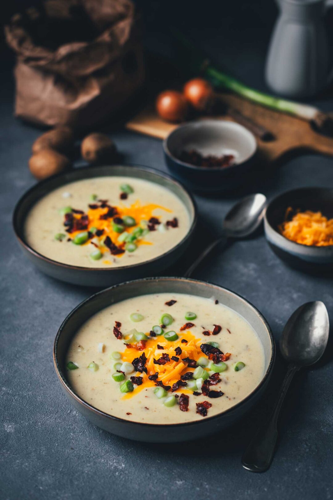 Cremige Kartoffelsuppe mit knusprigem Bacon, geschmolzenem Cheddar und Frühlingszwiebeln in einer dunklen Keramikschale – wärmendes Suppenrezept für Herbst und Winter. | moeyskitchen.com