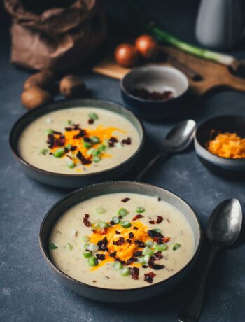 Cremige Kartoffelsuppe mit knusprigem Bacon, geschmolzenem Cheddar und Frühlingszwiebeln in einer dunklen Keramikschale – wärmendes Suppenrezept für Herbst und Winter. | moeyskitchen.com