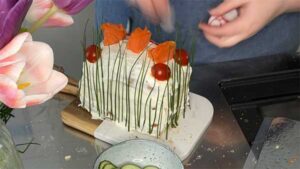 Die Sandwichtorte wird final mit Tomaten, Gurken, Radieschen und Räucherlachs dekoriert
