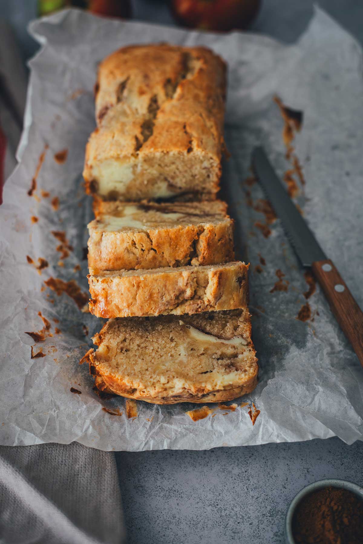 Seitliche Aufnahme vom Apfel-Frischkäse-Kuchen. In Scheiben geschnittener Kastenkuchen. Man erkennt die Frischkäse-Schichte und den Zimt-Swirl im Teig | moeyskitchen.com