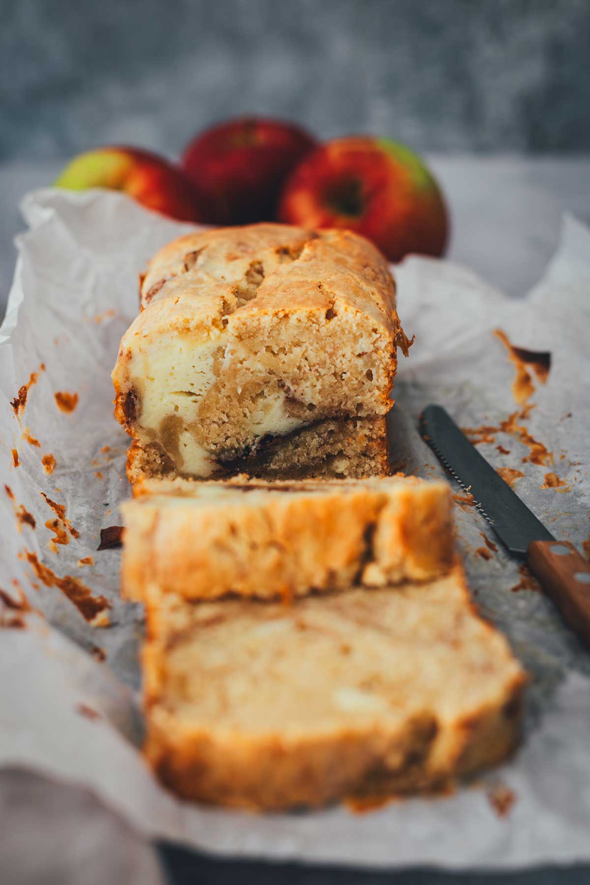 Nahaufnahme des angeschnittenen Apfel-Frischkäse-Kuchens auf Backpapier mit einem Brotmesser | moeyskitchen.com