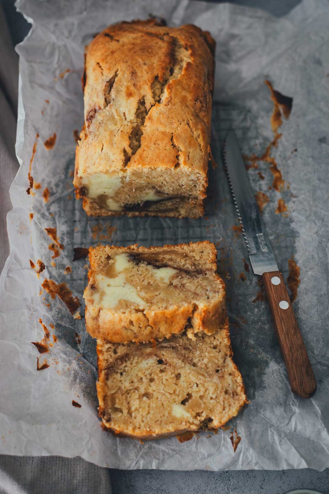 In Stücke geschnittener Apfel-Frischkäse-Kuchen auf Backpapier mit einem Messer | moeyskitchen.com