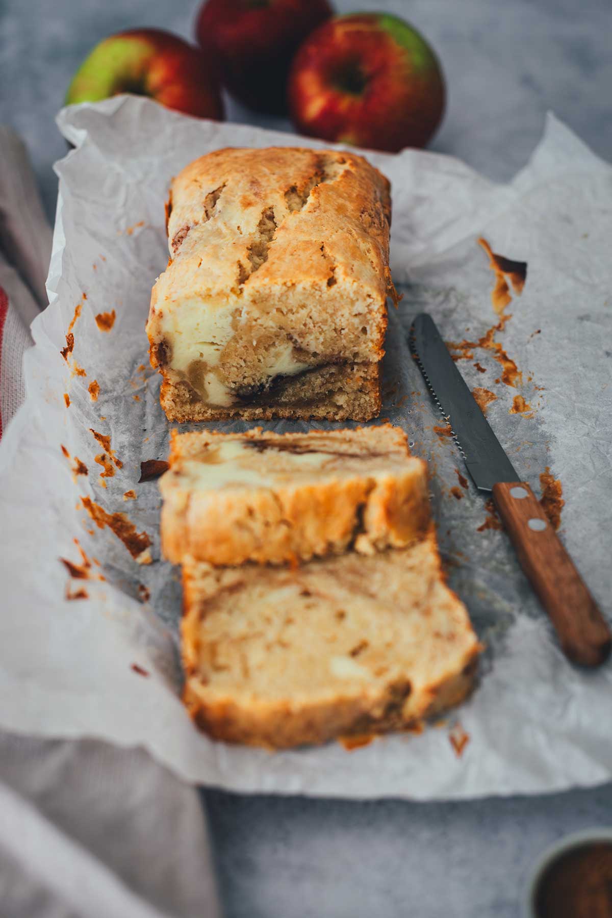Zwei Scheiben eines Apfelkuchens mit Frischkäse. Man sieht den Kastenkuchen, Backpapier und ein Messer. | moeyskitchen.com