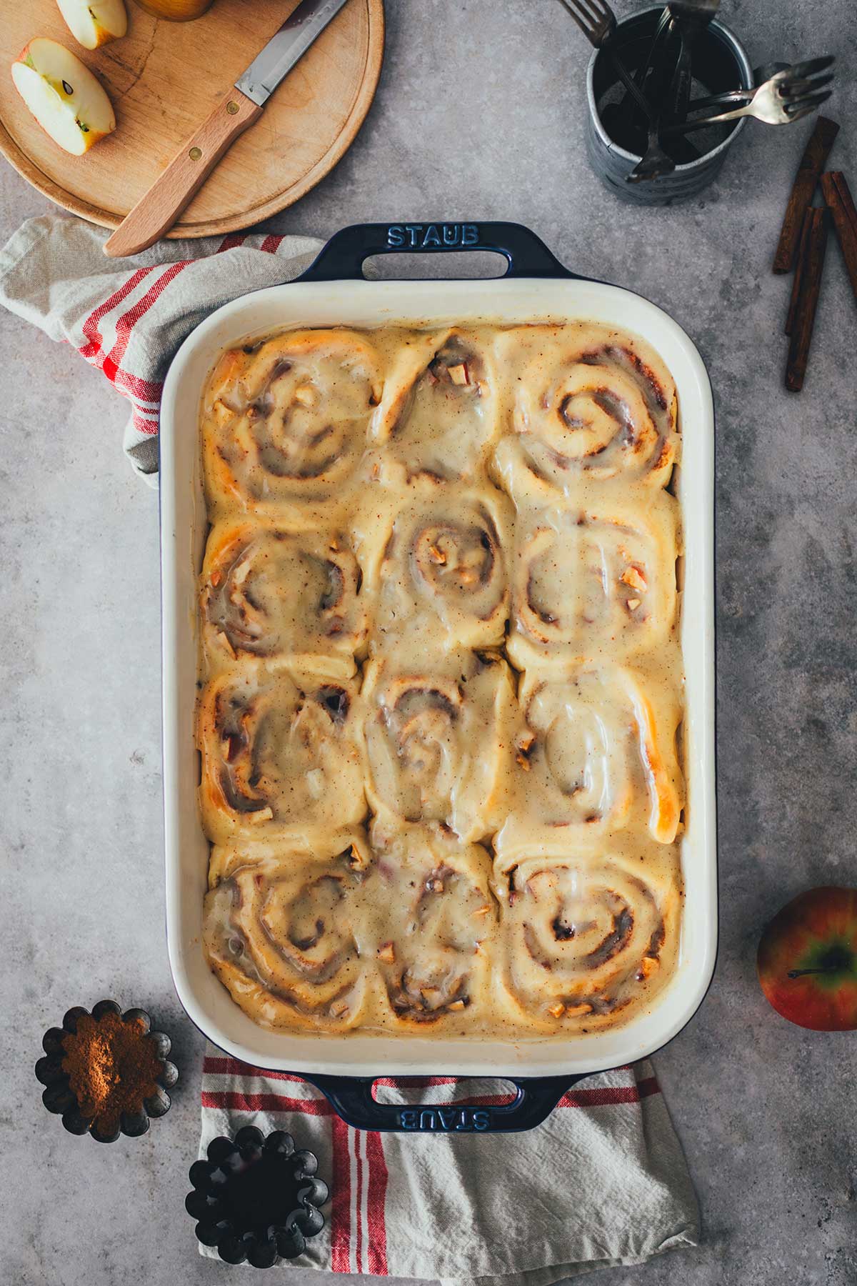 Topshot der Backform mit Apple Cinnamon Rolls – fertig gebacken in der Backform. Daneben sieht man Zimt und einen angeschnittenen Apfel. | moeyskitchen.com