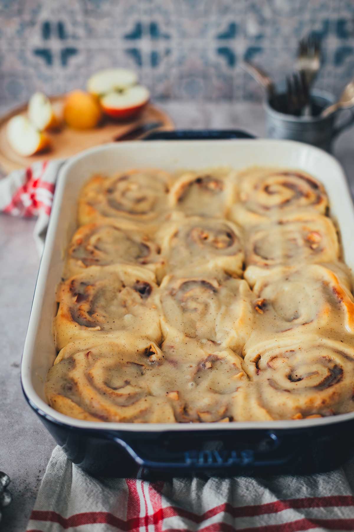 Seitliche Perspektive direkt auf eine Backform, gefüllt mit Apfel-Zimtschnecken, noch nicht angeschnitten, aber mit Glasur drauf | moeyskitchen.com