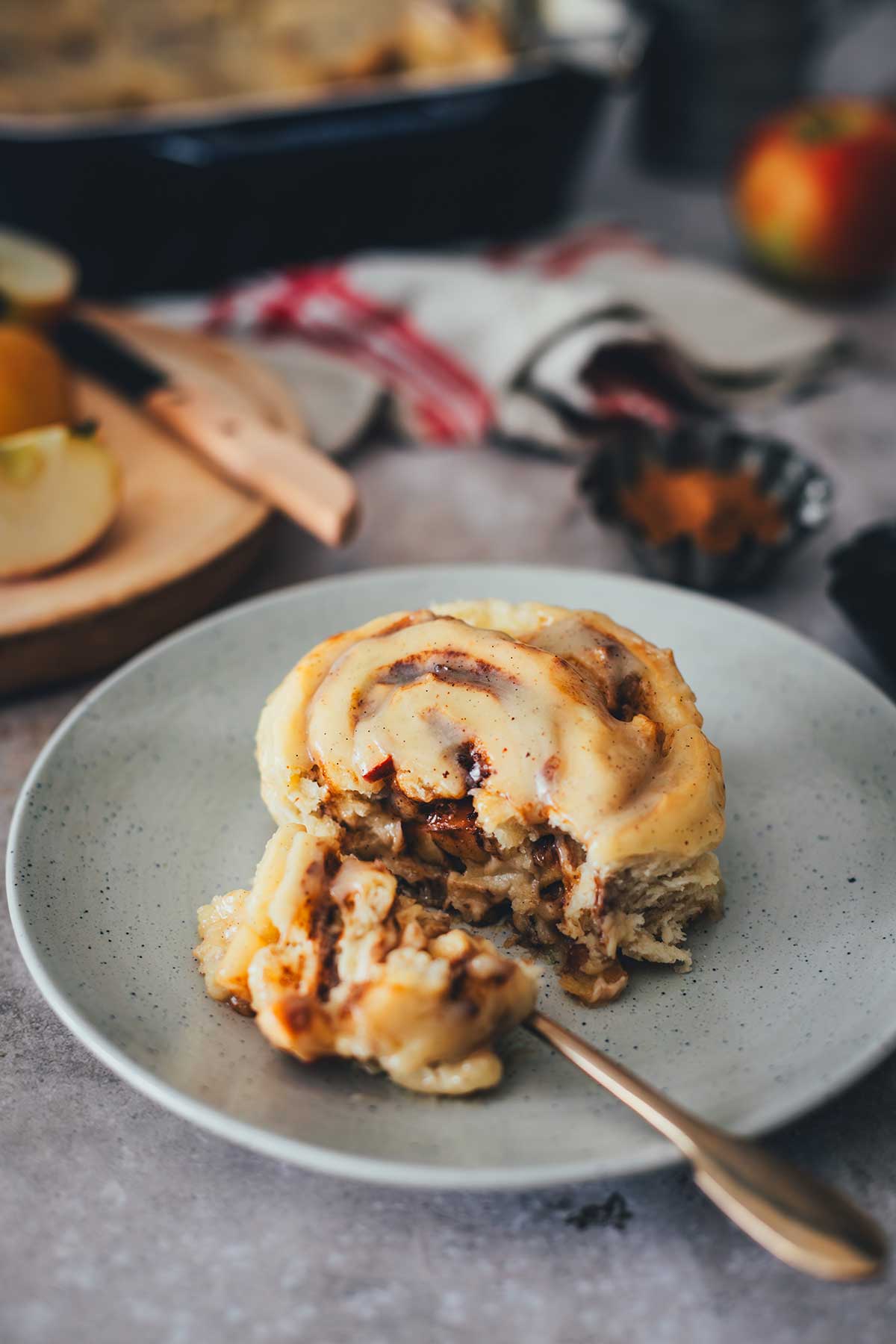 seitlicher Anschnitt: eine Apfel-Zimtschnecke auf einem Teller in Nahaufnahme. Mit einer Gabel wurde ein Stück abgenommen und man sieht die saftige Füllung | moeyskitchen.com