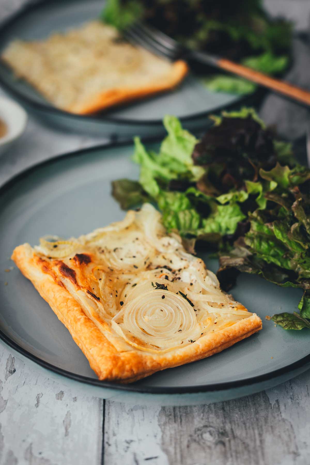 Detailaufnahme: Stück Zwiebeltarte mit Zwiebeln auf Teller mit grünem Salat | moeyskitchen.com