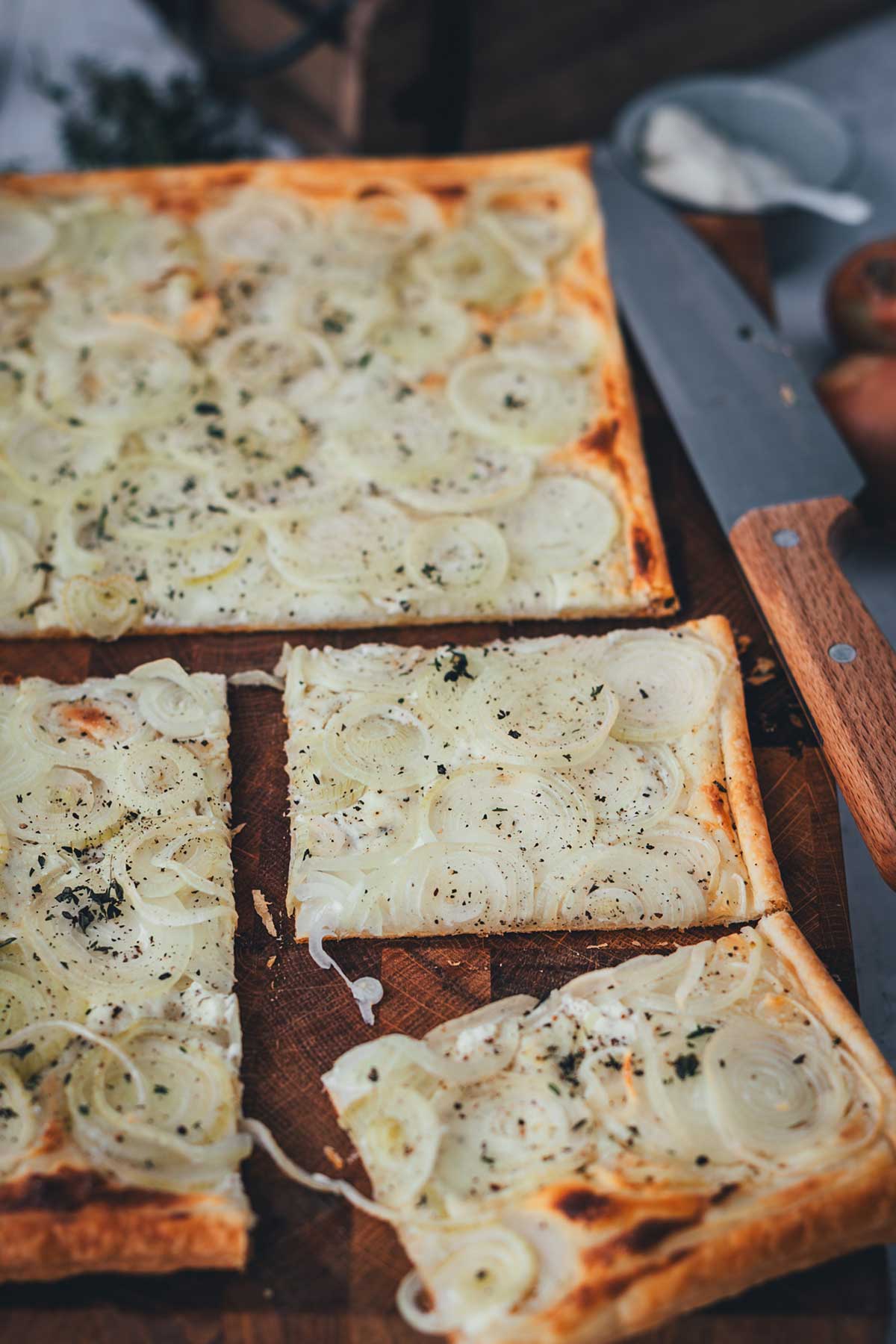 Aufgeschnittene Zwiebeltarte auf Holzbrett mit knusprigem Blätterteig und Zwiebeln | moeyskitchen.com
