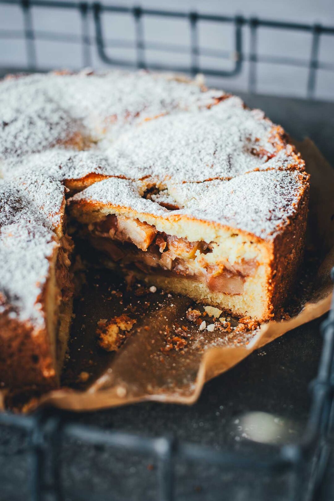 Appeltaart – niederländischer Apfelkuchen am Stück auf einem Stück Backpapier auf einem Tabelett serviert. Man sieht die saftige Füllung des angeschnittenen Kuchens | moeyskitchen.com