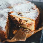 Appeltaart – niederländischer Apfelkuchen am Stück auf einem Stück Backpapier auf einem Tabelett serviert. Man sieht die saftige Füllung des angeschnittenen Kuchens | moeyskitchen.com