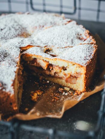 Appeltaart – niederländischer Apfelkuchen am Stück auf einem Stück Backpapier auf einem Tabelett serviert. Man sieht die saftige Füllung des angeschnittenen Kuchens | moeyskitchen.com