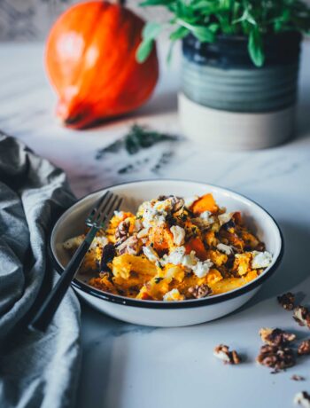 Seitliche Ansicht eines Tellers mit einem Pastagericht – cremige Kürbis-Feta-Pasta, bestreut mit Walnüssen. Im Hintergrund liegt ein Hokkaido-Kürbis, daneben ein Topf mit Salbei. Im Vordergrund sieht man eine Serviette und Walnusskerne. | moeyskitchen.com