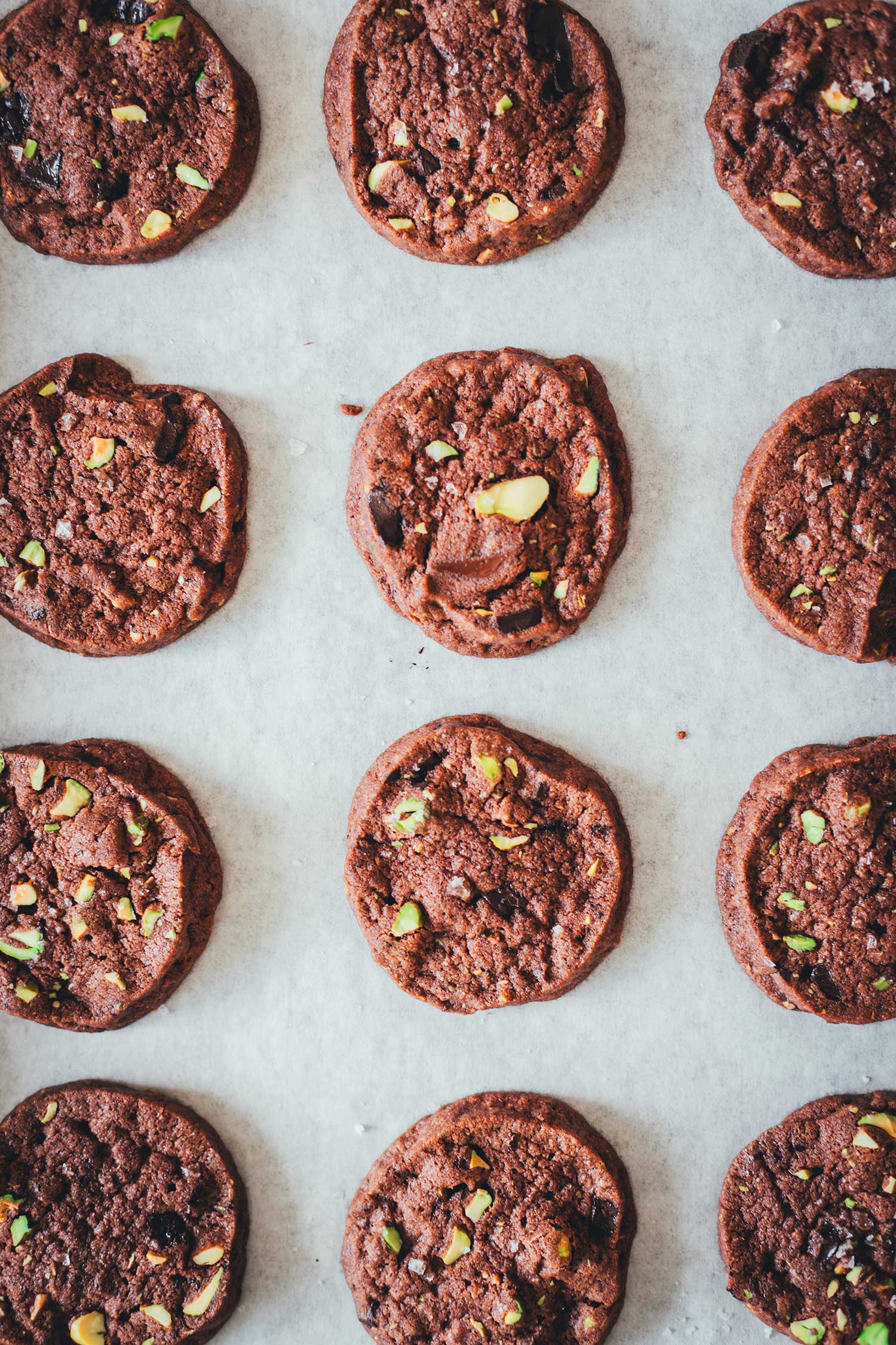 Topshot Nahaufnahme von Schokoladenkeksen mit Pistazien und Meersalz, auf einem Backblech liegend