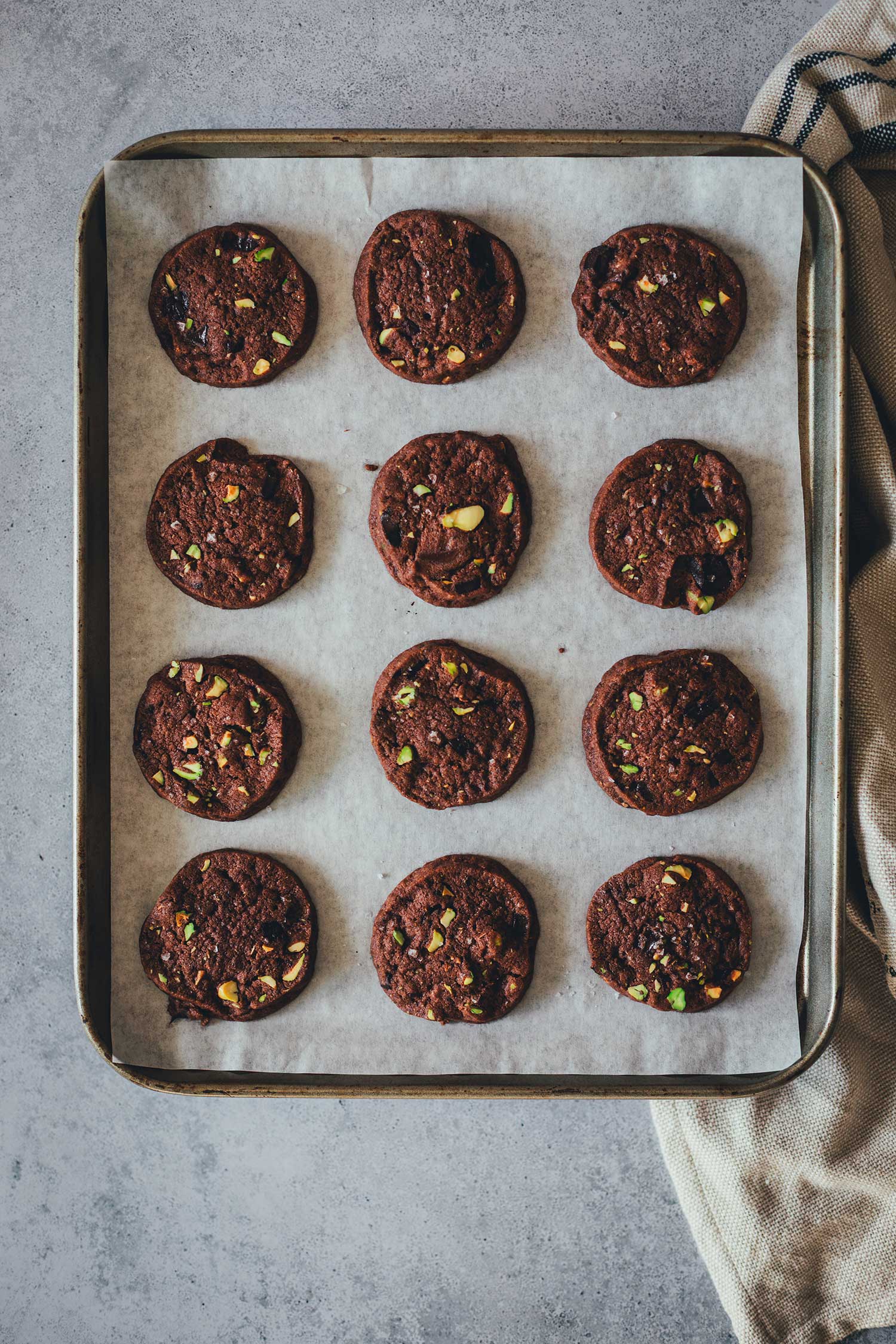 Topshot Aufnahme der fertig gebackenen Schokoladen-Pistazien-Cookies auf einem mit Backpapier ausgelegten Backblech