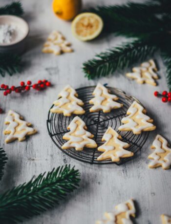 Seitliche Ansicht von Zitronenplätzchen mit Zuckergus inn Form von Tannenbäumchen auf einem kleinen Kuchengitter mit weihnachtlicher Dekoration drumherum | moeyskitchen.com