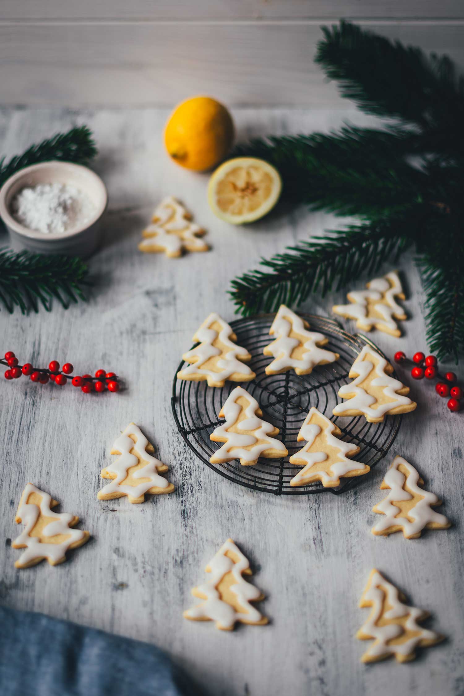 Seitliche Ansicht von Zitronenplätzchen mit Zuckergus inn Form von Tannenbäumchen auf einem kleinen Kuchengitter mit weihnachtlicher Dekoration drumherum | moeyskitchen.com