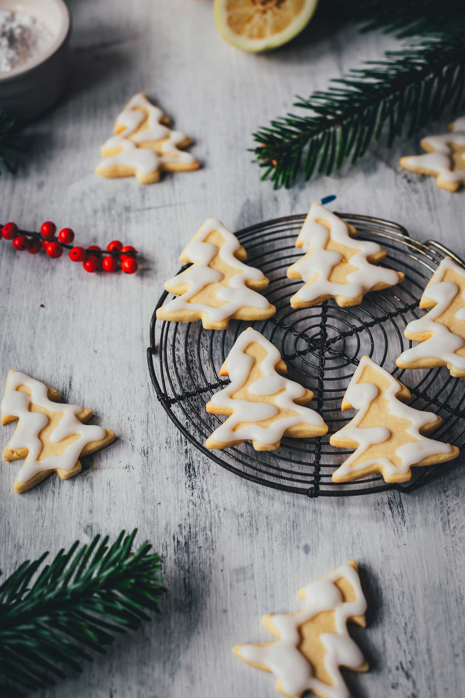 Seitliche Ansicht von Zitronenplätzchen mit Zuckergus inn Form von Tannenbäumchen auf einem kleinen Kuchengitter mit weihnachtlicher Dekoration drumherum | moeyskitchen.com
