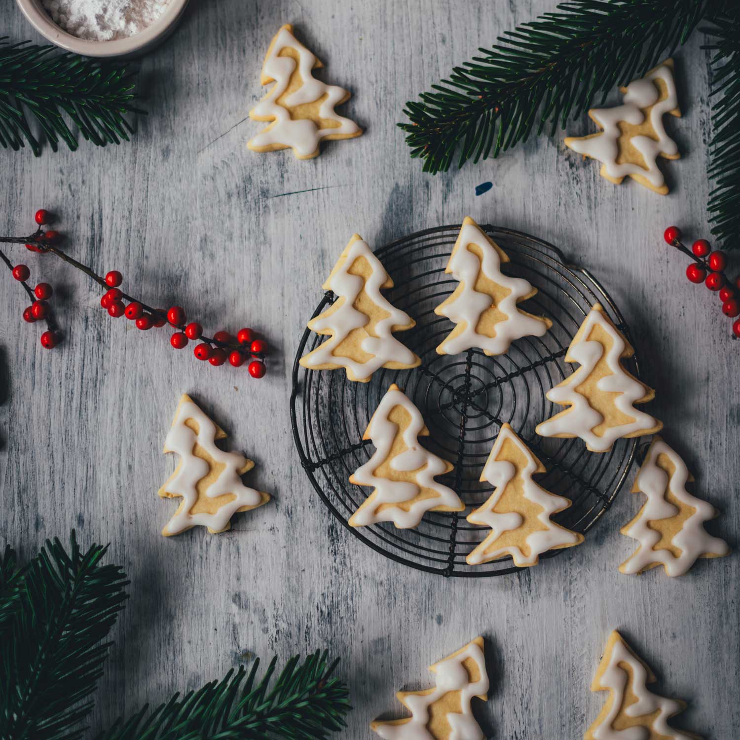 Topshot von Zitronenplätzchen in Form von kleinen Tannenbäumchen, mit Zuckerguss verziert, der aussieht, als wären die Bäumchen eingeschneit | moeyskitchen.com