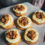 Brown Butter Apple Pie Cookies auf einem Tablett, frisch dekoriert mit Mascarpone-Frosting und Apfeltopping; im Hintergrund unscharfer Arm einer Person beim Servieren.