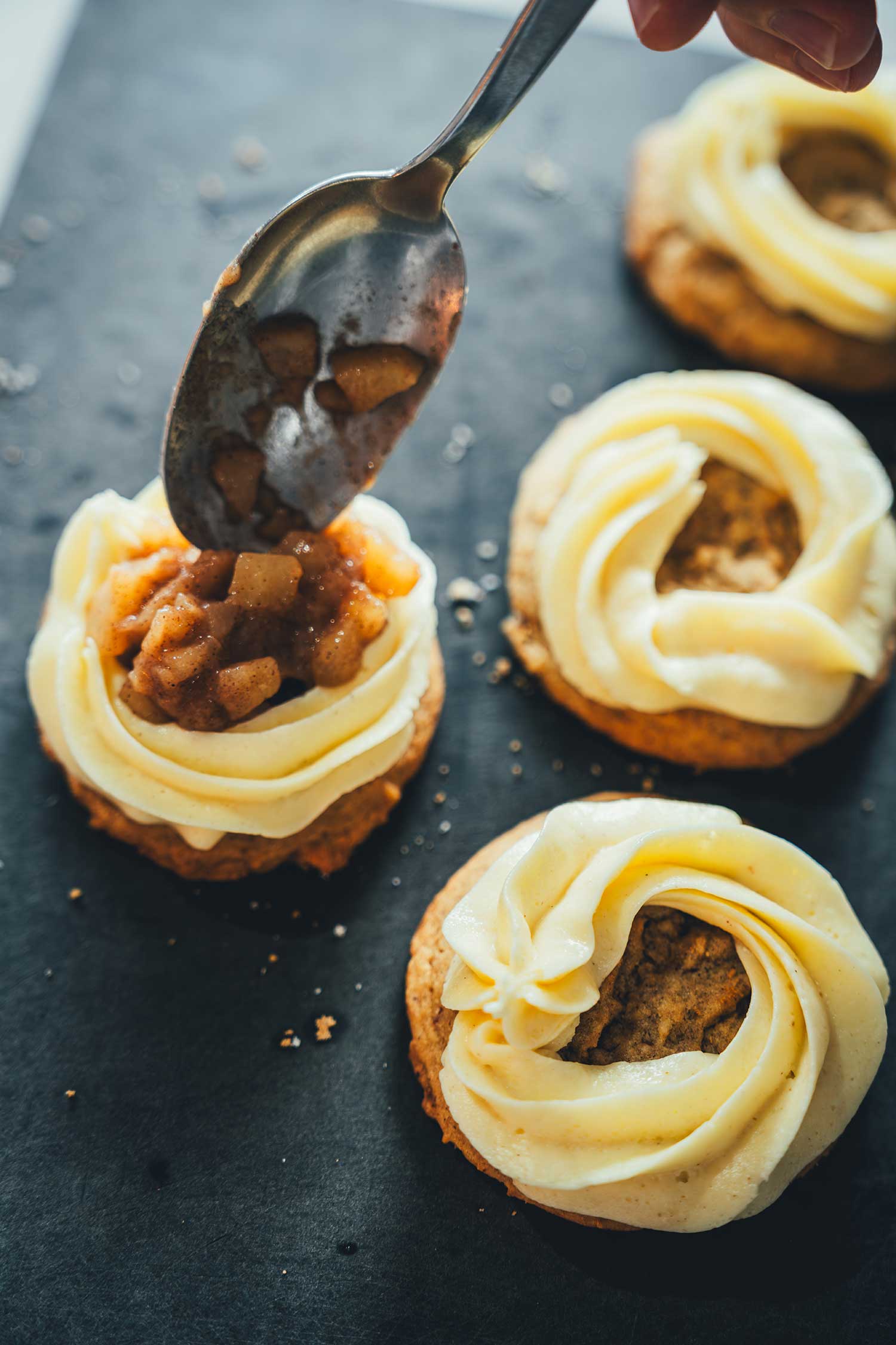 Apfeltopping wird mit einem Esslöffel auf den Applie Pie Cookies verteilt, nachdem das Frosting auf die Cookies aufgespritzt wurde