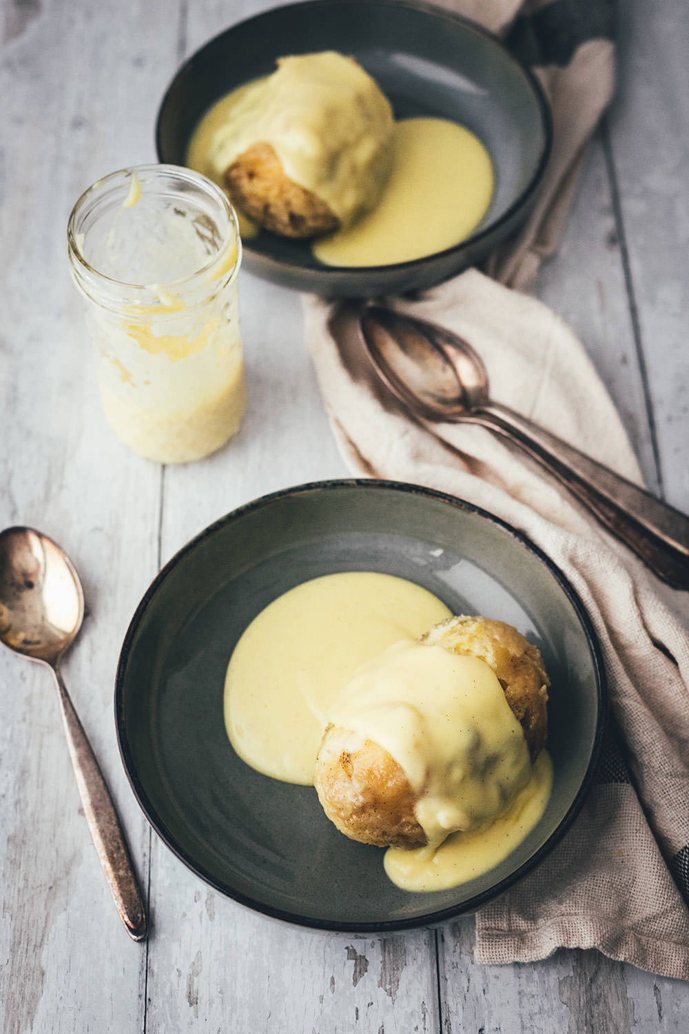 Zwei fluffige, goldbraun ausgebackene Dampfnudeln in dunklen Schalen, großzügig übergossen mit einer cremigen, hellgelben Vanillesauce – eines meiner liebsten Rezepte für den Februar.