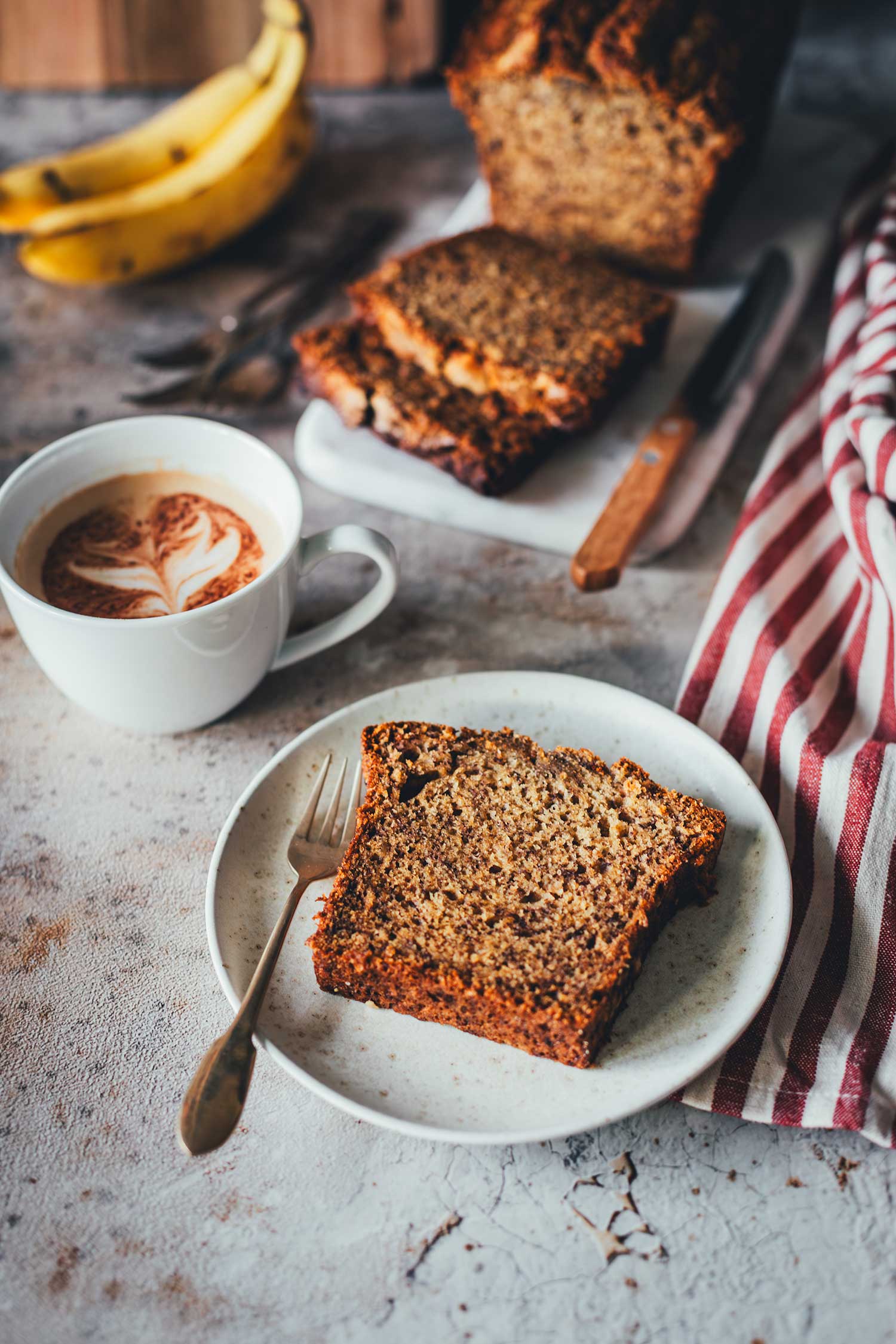 Bananenbrot auf Teller mit Kaffee und Banane im Hintergrund