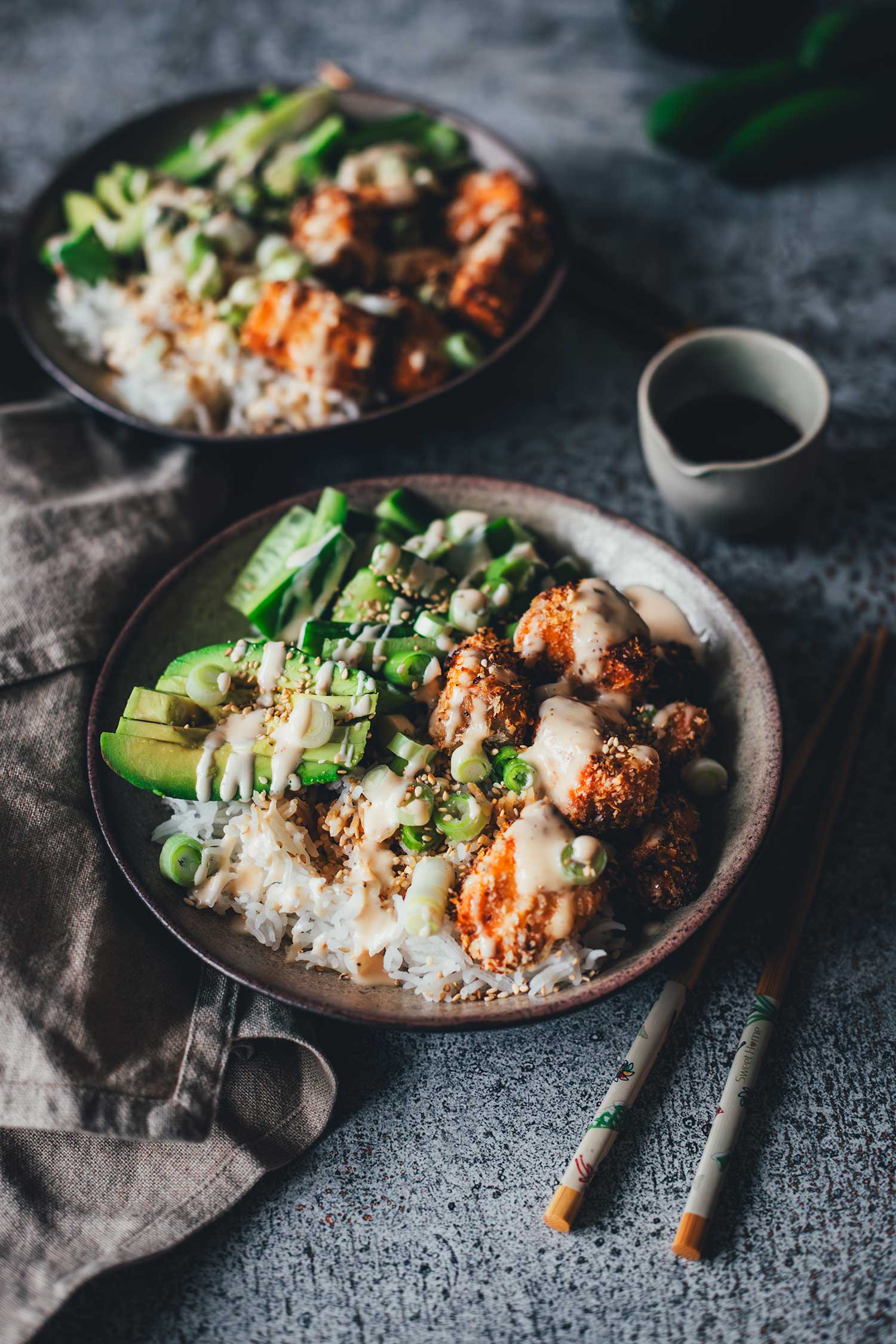 Nahaufnahme einer Crispy Lachs Bowl mit Fokus auf knusprigem Lachs, frischer Avocado, Gurkenscheiben und cremigem Dressing
