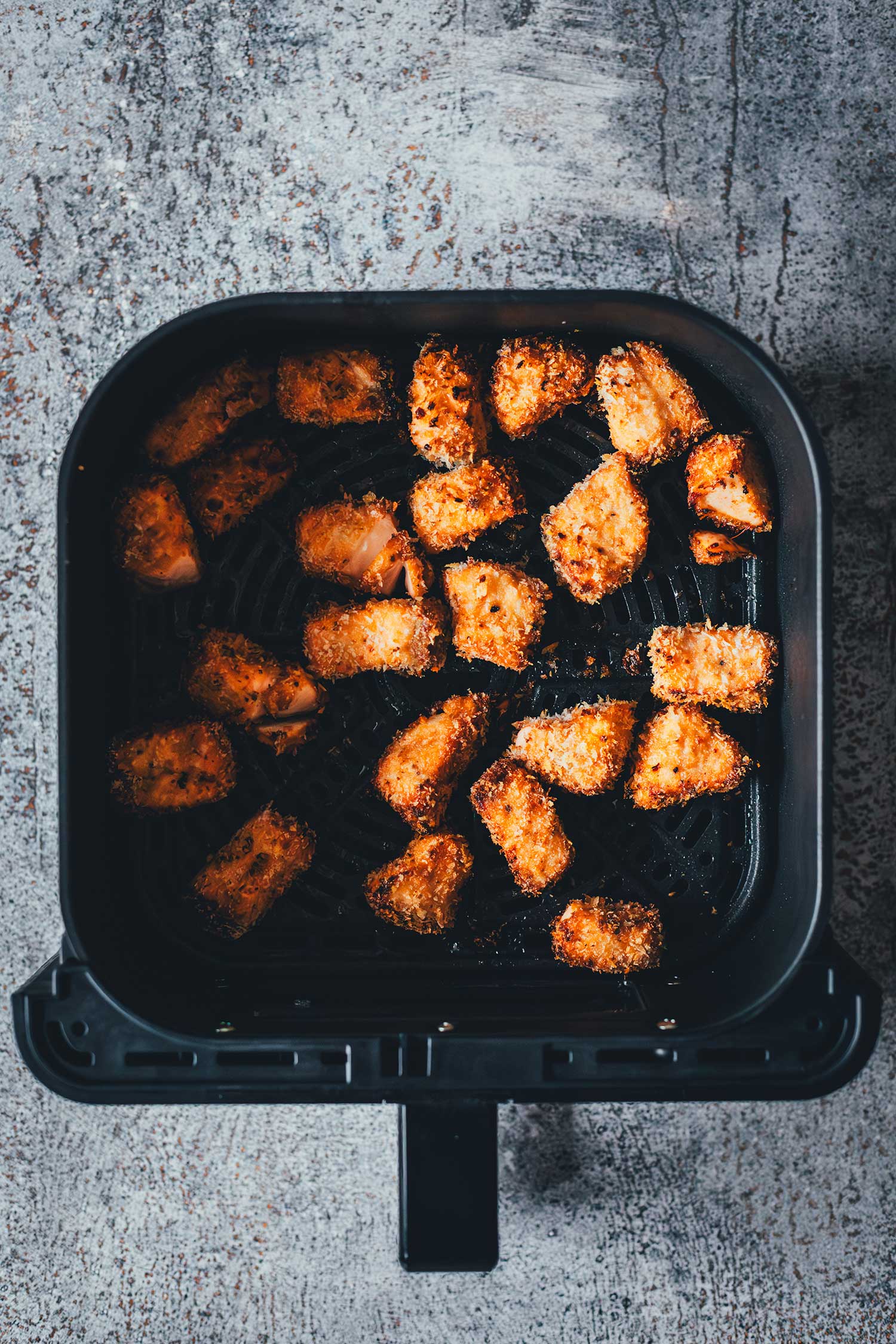 Fertig gegarte, goldbraune und knusprige Lachswürfel mit Panko-Panade im Korb der Heißluftfritteuse