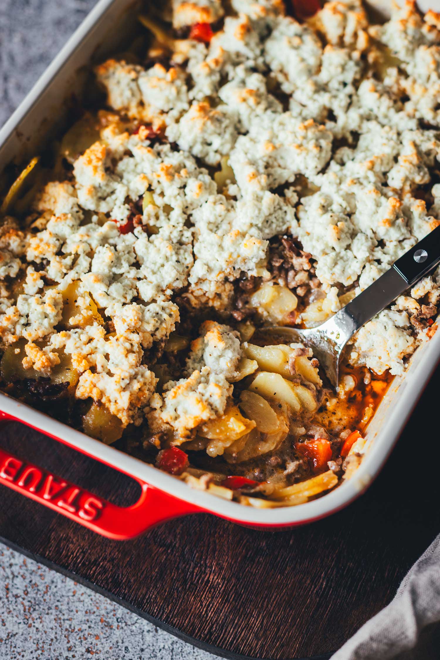 Nahaufnahme eines herzhaften Auflaufs mit Hackfleisch und Kartoffelscheiben, bedeckt mit einer goldbraun überbackenen Schicht aus zerbröseltem Feta.
