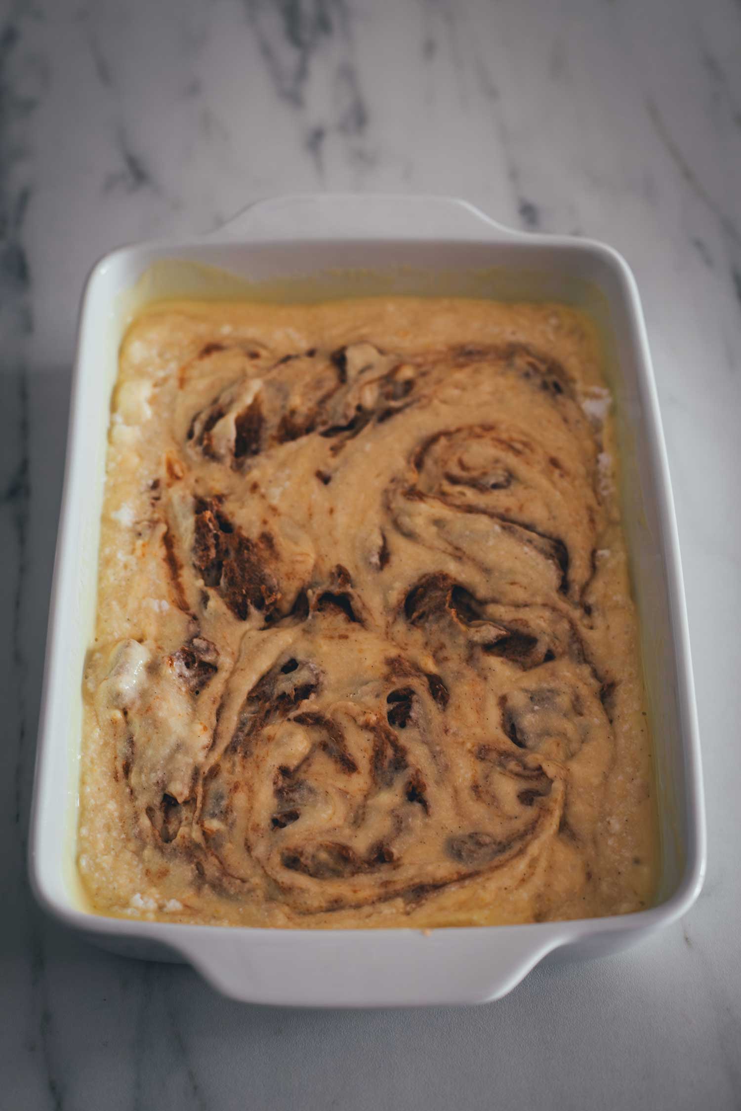 Der Teig für den Zimtschnecken-Kuchen ohne Hefe in der Backform, die Zimtfüllung ist leicht marmomiert – bereit für den Backofen.