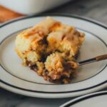 Nahaufnahme eines Stücks vom Zimtschnecken-Kuchen ohne Hefe auf einem Teller. Eine Gabel hat ein Stück abgenommen und man sieht die saftige und lockere Textur.