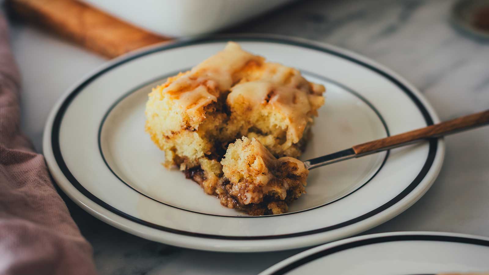 Nahaufnahme eines Stücks vom Zimtschnecken-Kuchen ohne Hefe auf einem Teller. Eine Gabel hat ein Stück abgenommen und man sieht die saftige und lockere Textur.