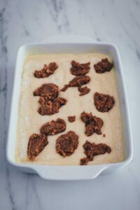 Der Teig für den Zimtschnecken-Kuchen ohne Hefe ist in der Backform und mit Zimtfüllung bedeckt, bevor er leicht marmomiert wird.