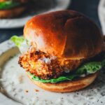 Crispy Chicken Burger Caesar-Style aus dem Airfryer mit knuspriger Panko-Kruste und Romanasalat im Brioche-Bun, dazu Caesar-Sauce auf gepunktetem Teller