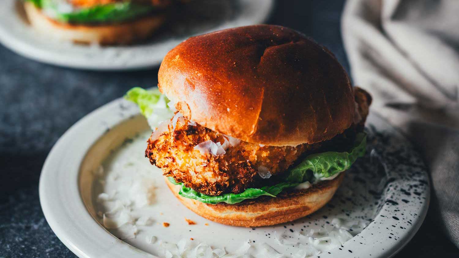 Crispy Chicken Burger Caesar-Style aus dem Airfryer mit knuspriger Panko-Kruste und Romanasalat im Brioche-Bun, dazu Caesar-Sauce auf gepunktetem Teller