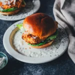 Crispy Chicken Burger Caesar-Style aus dem Airfryer mit knuspriger Panko-Kruste und Romanasalat im Brioche-Bun, dazu Caesar-Sauce auf gepunktetem Teller