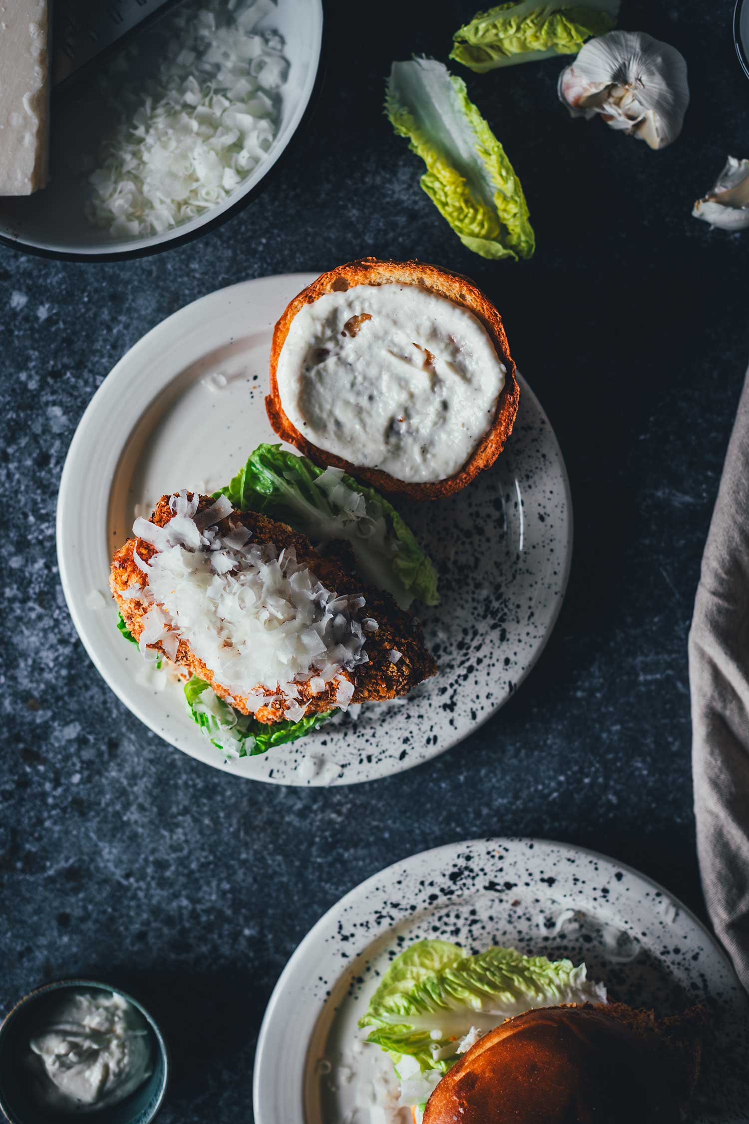 Aufnahme von oben auf einen geöffneten Crispy Chicken Burger mit knusprigem Hähnchen, Parmesan-Spänen und Caesar-Sauce auf dem getoasteten Bun