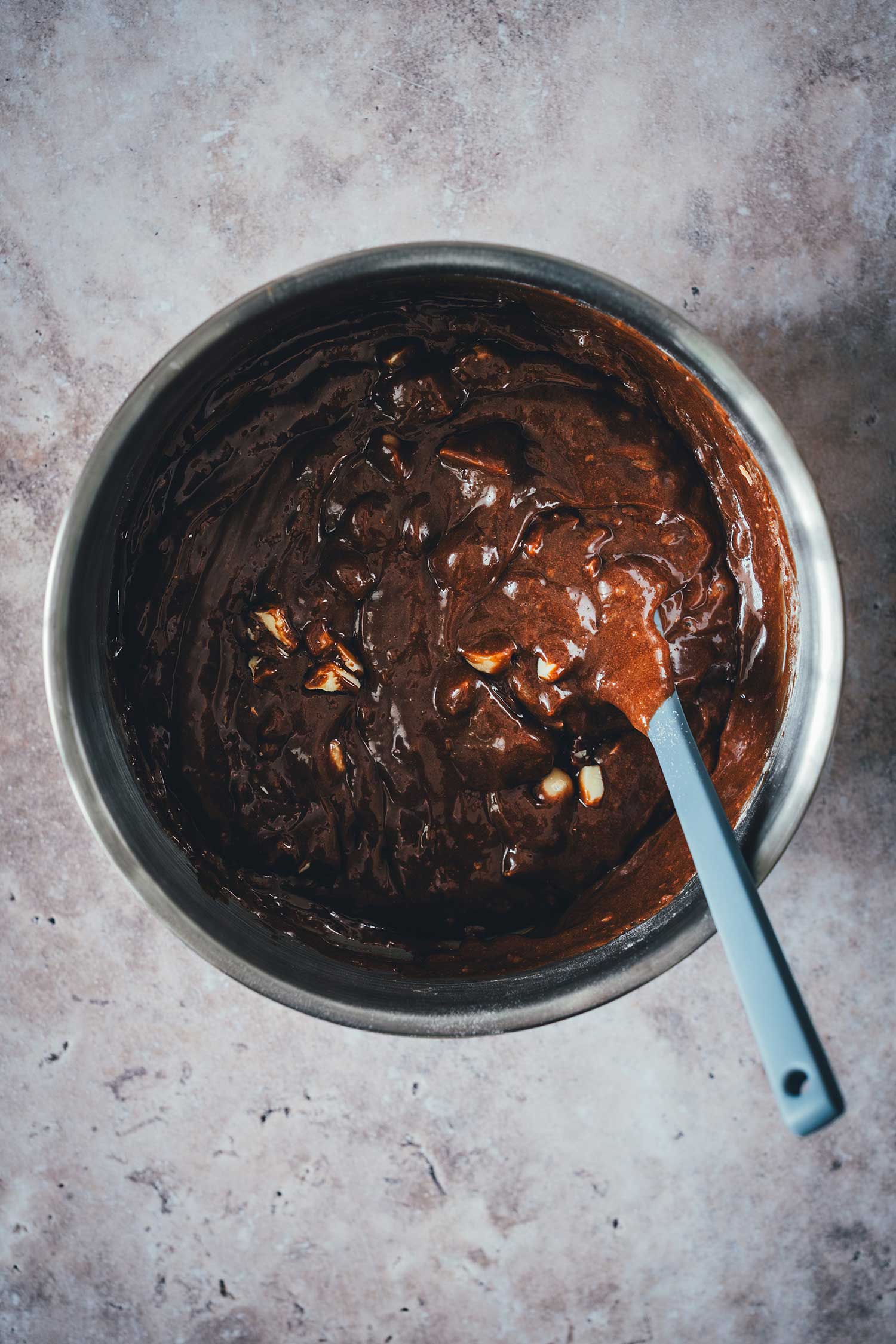 Fertig vermischter Brownie-Teig mit untergehobenen Macadamias und weißer Schokolade in einer Edelstahlschüssel.