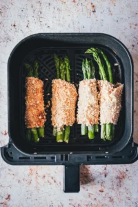 Vier panierte Spargel-Cordon-Bleu-Päckchen mit Panko-Kruste im Airfryer-Korb vor dem Garen