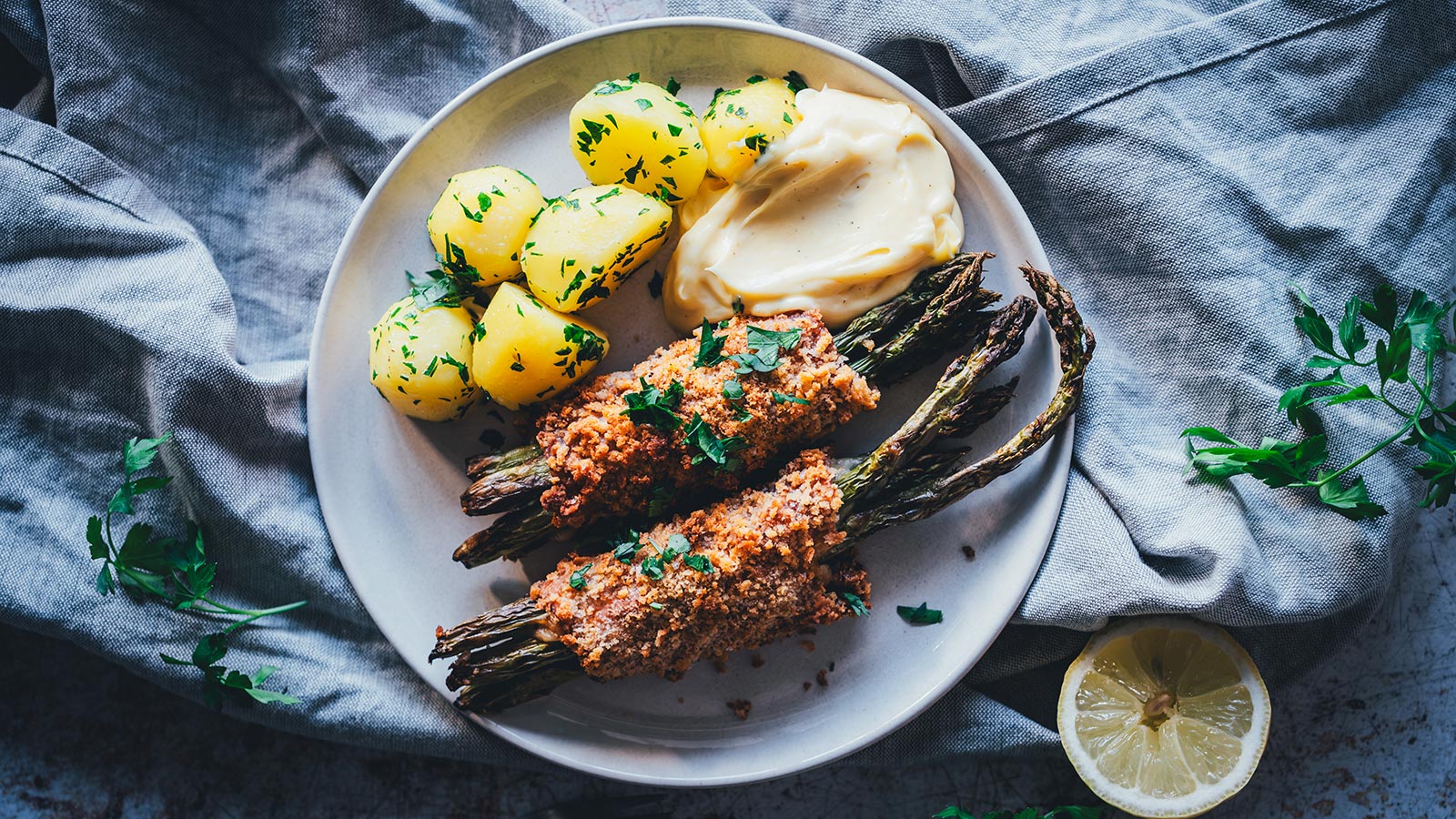 Spargel Cordon Bleu mit grünem Spargel, Hollandaise und Petersilienkartoffeln auf hellem Teller von oben