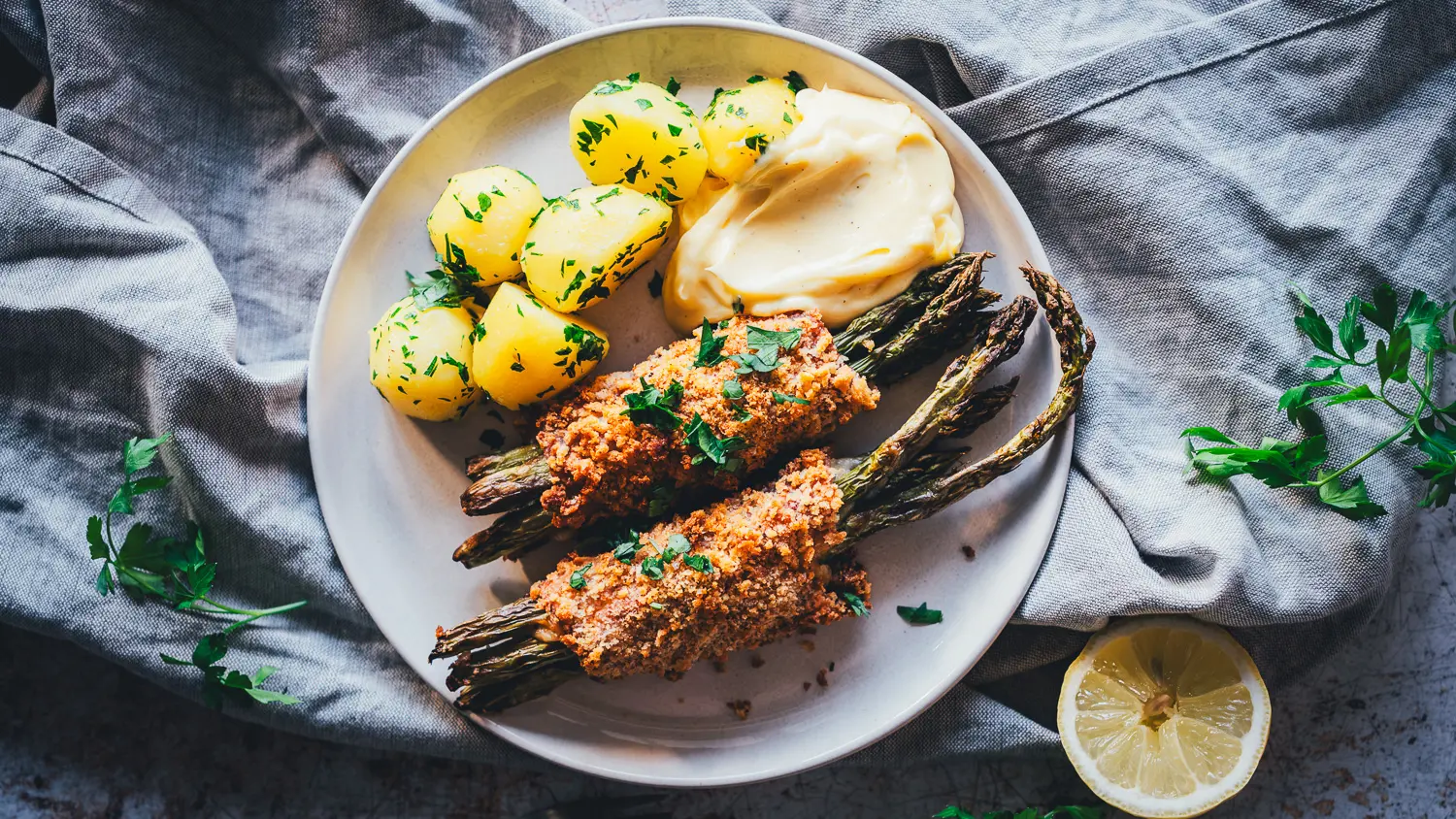 Spargel Cordon Bleu mit grünem Spargel, Hollandaise und Petersilienkartoffeln auf hellem Teller von oben