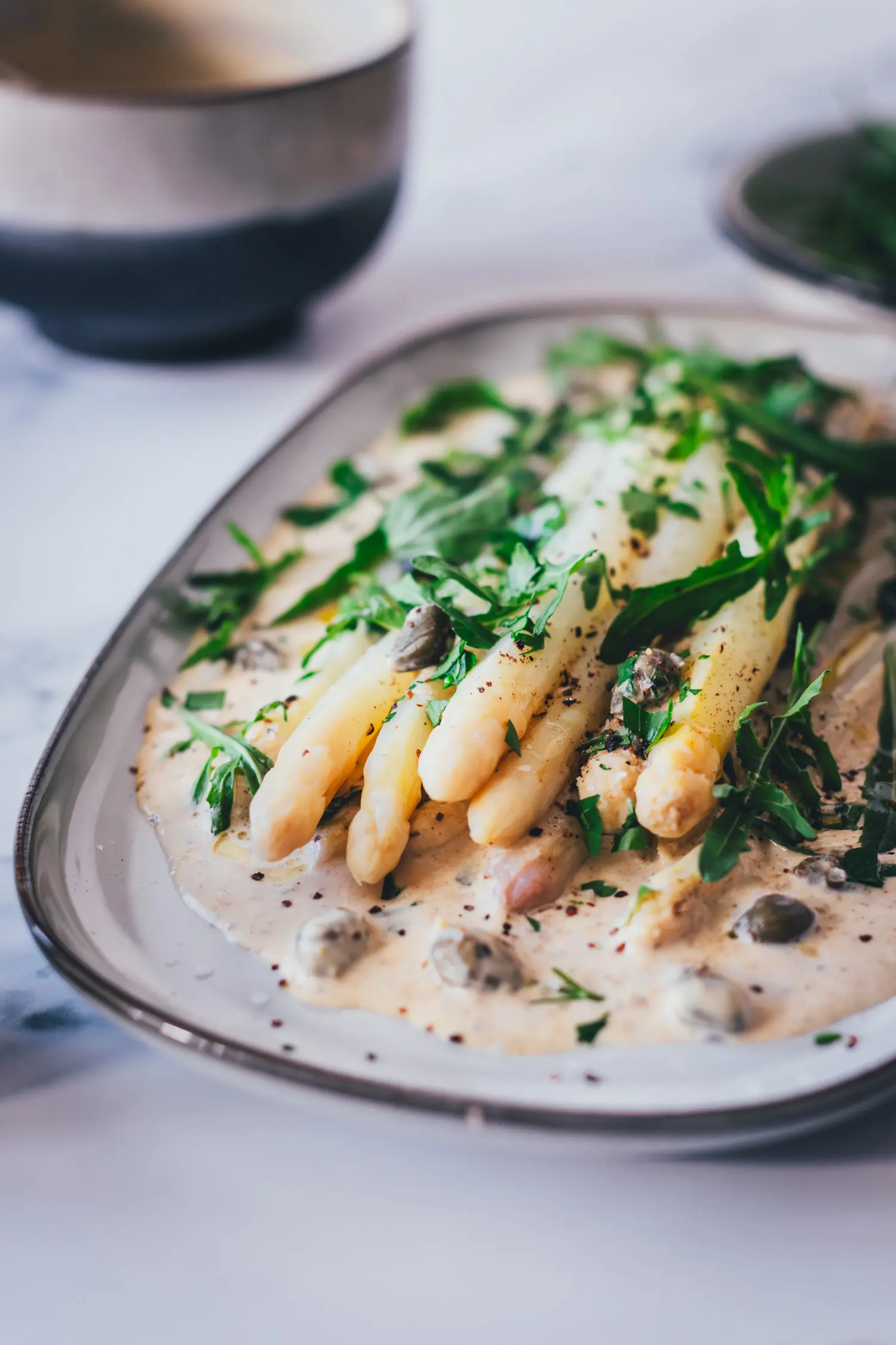 Spargel Tonnato als italienische Vorspeise angerichtet: zart gegarter weißer Spargel auf Thunfischsauce mit Kapern und Rucola, Detailaufnahme