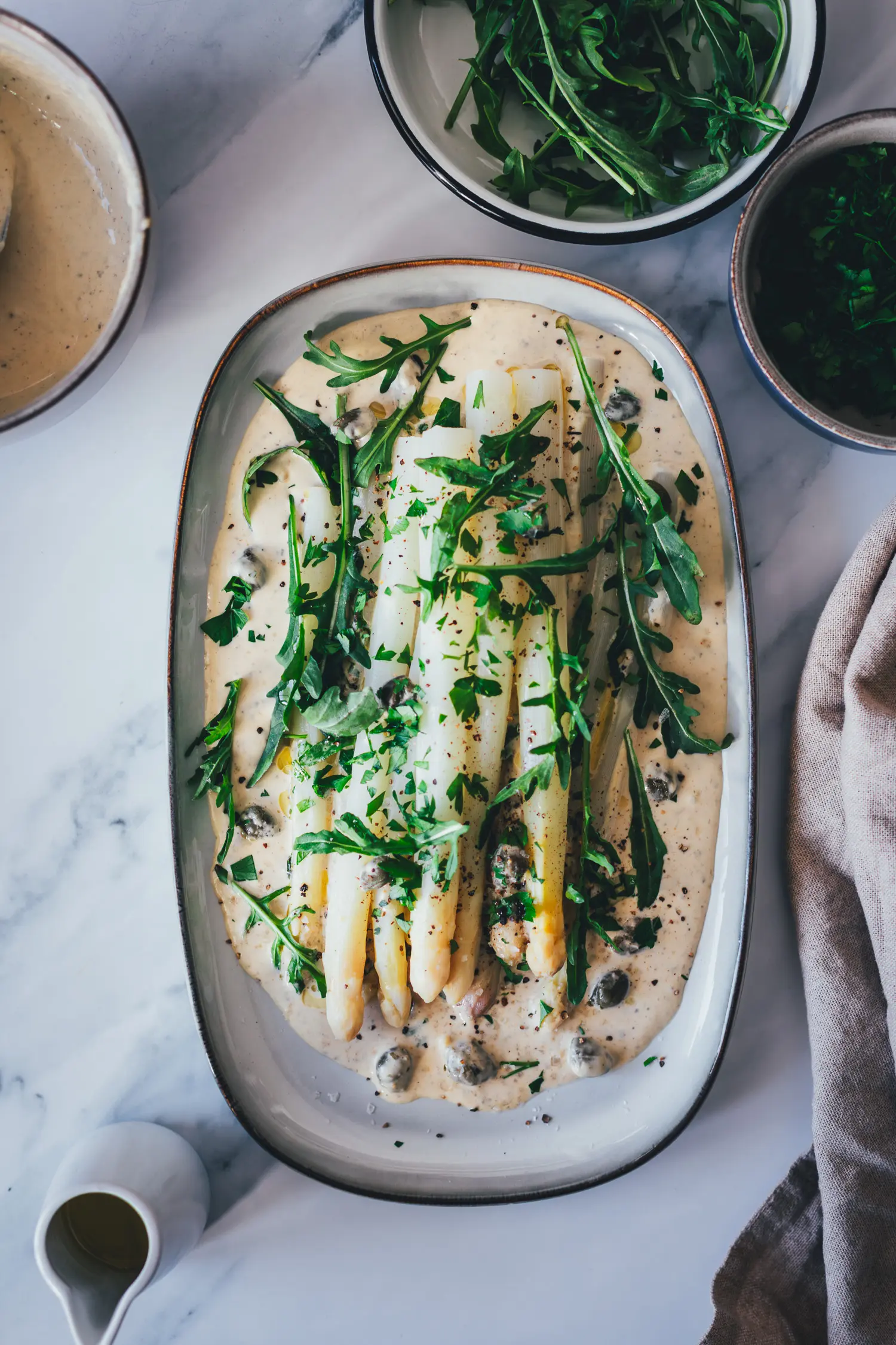 Spargel Tonnato von oben fotografiert: weißer Spargel auf samtiger Tonnatosauce mit Rucola, frischen Kräutern und Kapern garniert