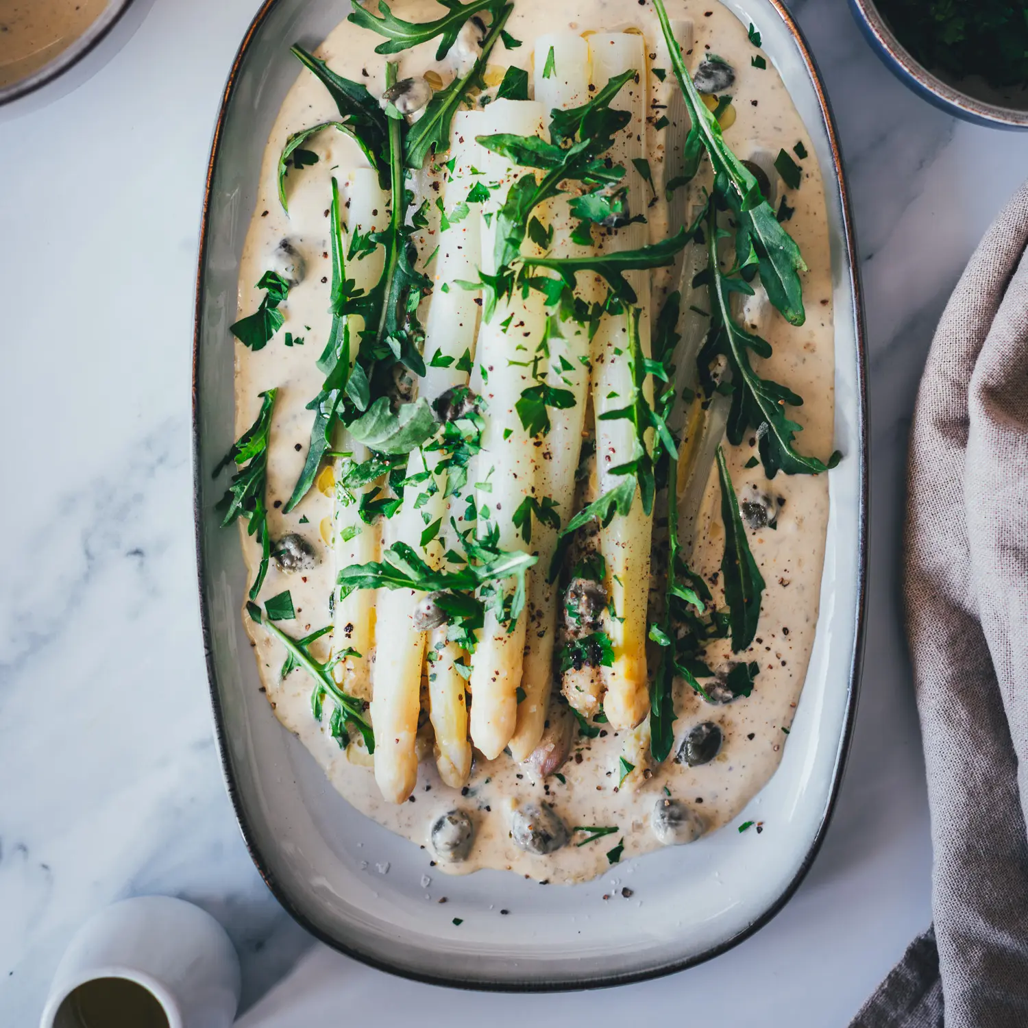 Spargel Tonnato Topshot: weißer Spargel auf cremiger italienischer Thunfischsauce, garniert mit Rucola, Kapern und Petersilie