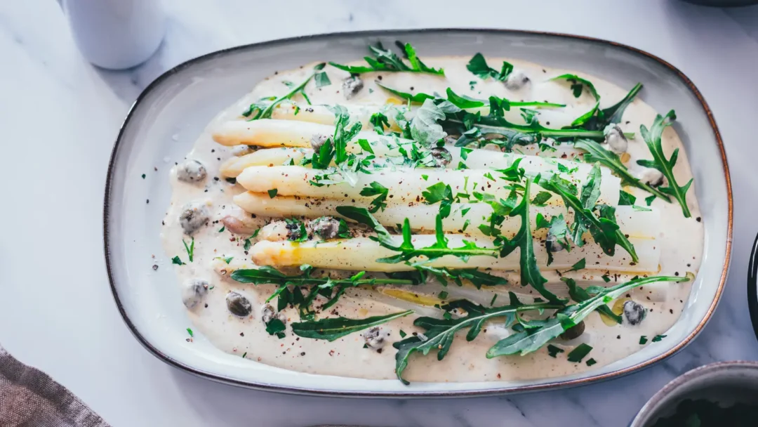 Spargel Tonnato mit weißem Spargel auf cremiger italienischer Thunfischsauce, garniert mit Rucola, Kapern und Petersilie auf ovaler Servierplatte