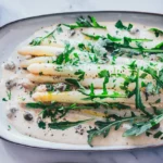 Spargel Tonnato mit weißem Spargel auf cremiger italienischer Thunfischsauce, garniert mit Rucola, Kapern und Petersilie auf ovaler Servierplatte